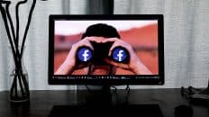 Pantala de un computador que muestra a una persona mirando por unos binoculares con el logo de Facebook