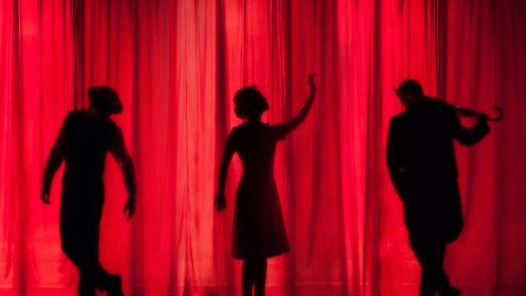 Tres siluetas de personas detrás de una cortina roja. Teatro para la inclusión de personas sordas