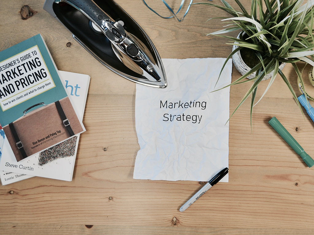 Hoja encima de una mesa que dice "marketing", también hay marcadores, libros, una planta y una plancha. Email marketing